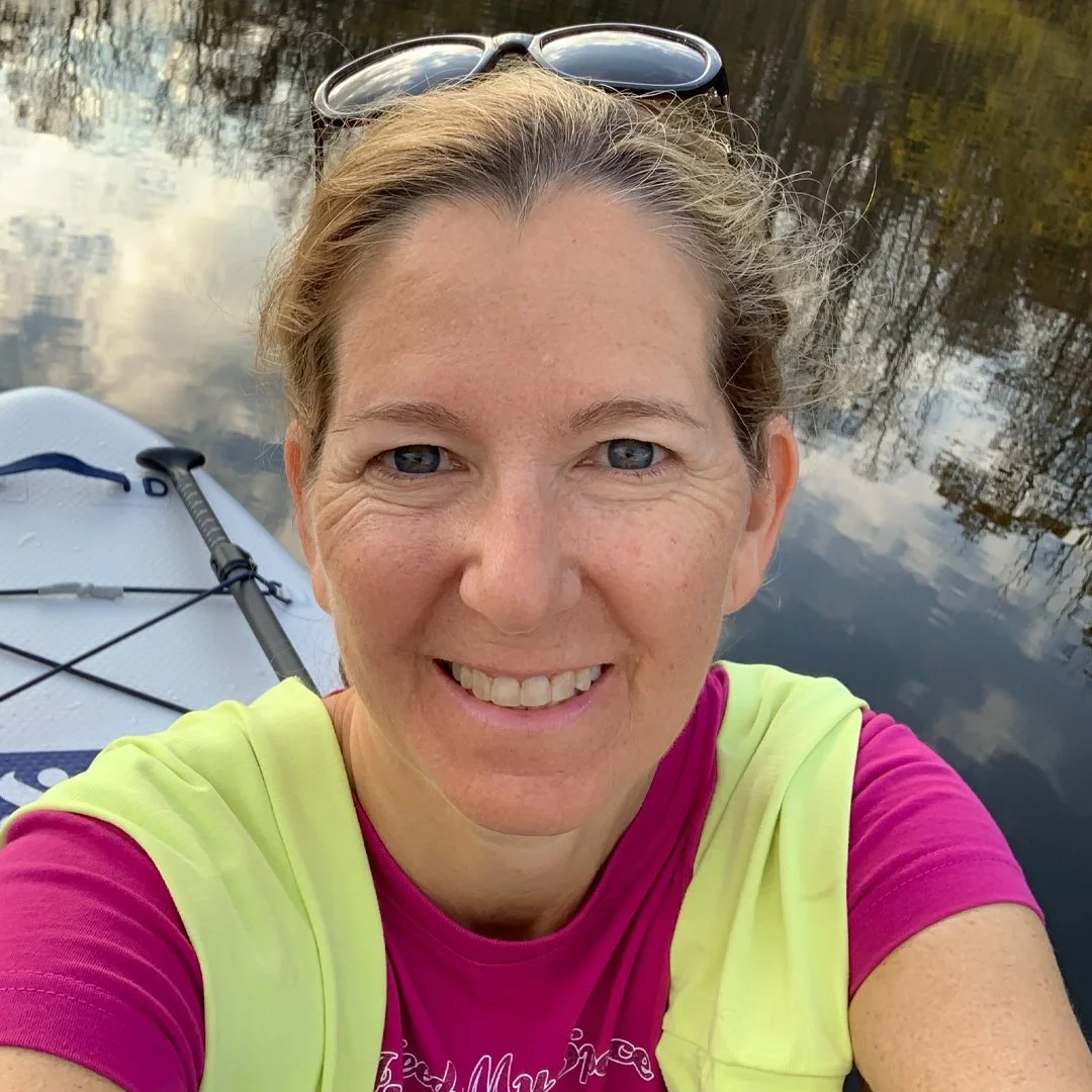 Person taking a selfie while paddleboarding on calm water.